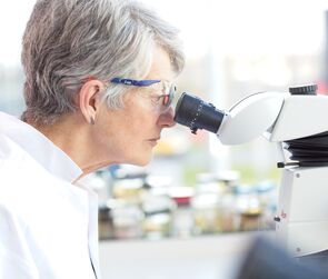 Woman in a lab coat looking into a microscope.